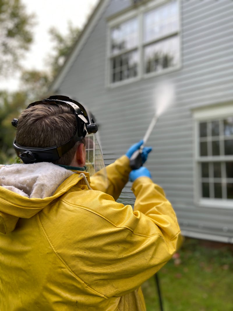 Person pressure washing a house
